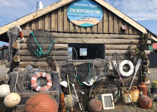 A rustic log cabin with a sign for a campground, surrounded by fishing gear, buoys, and nets.