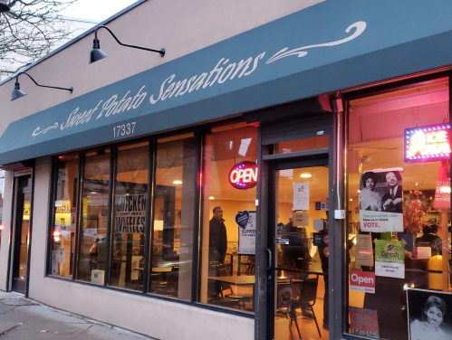 Exterior of "Sweet Potato Sensations" restaurant with large windows, an "Open" sign, and a cozy atmosphere.