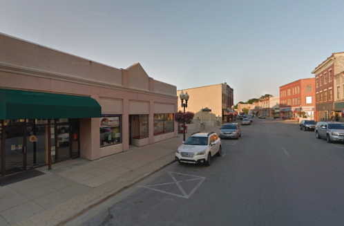 A quiet street scene featuring shops, parked cars, and a clear sky in a small town.