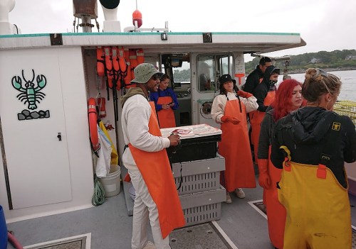 A group of people in orange fishing gear on a boat, preparing equipment and handling catch near the water.
