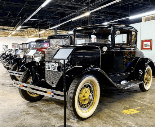 A vintage black car with gold wheels displayed in a museum alongside other classic cars.