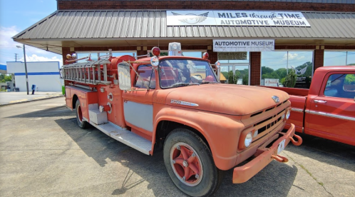 A vintage fire truck parked outside an automotive museum, showcasing its classic design and weathered paint.
