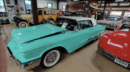 A vintage turquoise convertible car displayed in a classic car museum, surrounded by other antique vehicles.