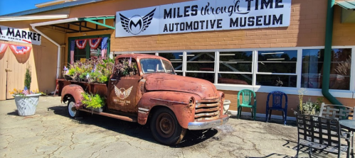 Rusty vintage truck with flowers in the bed, parked outside the Miles Through Time Automotive Museum.