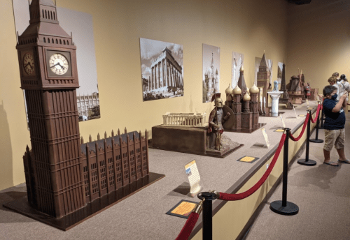 Chocolate sculptures of famous landmarks displayed in a museum setting, with visitors observing behind a red rope.