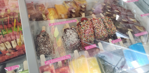 A display of colorful ice pops and paletas, including chocolate-covered options with sprinkles and coconut.