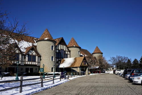 A stone building with turrets and a snowy landscape, alongside a parking lot filled with cars under a clear blue sky.