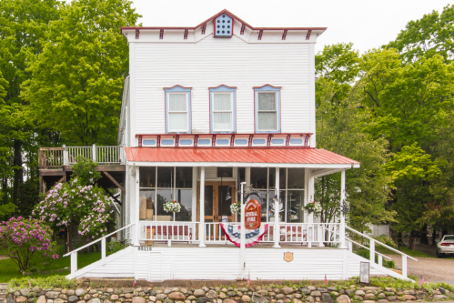 A charming white building with a red roof, surrounded by greenery and flowers, featuring a welcoming porch.
