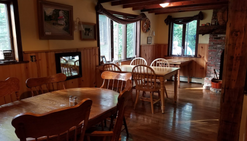 Cozy dining area with wooden tables and chairs, large windows, and rustic decor in a warm, inviting setting.