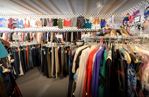 A clothing store interior filled with racks of colorful garments and a wall of hanging outfits.