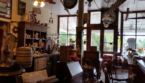 A cozy vintage shop filled with antiques, furniture, and decor, featuring large windows and warm lighting.
