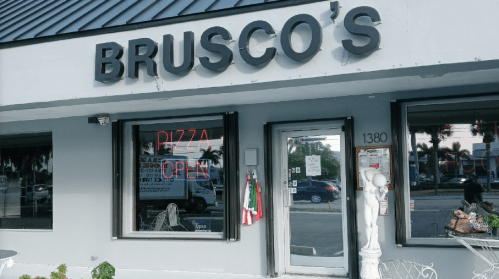 Exterior of Brusco's restaurant with a sign reading "Pizza Open" and a statue near the entrance.