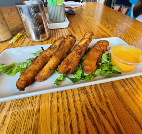 Plate of crispy fried zucchini sticks on a bed of lettuce, served with a small cup of dipping sauce.