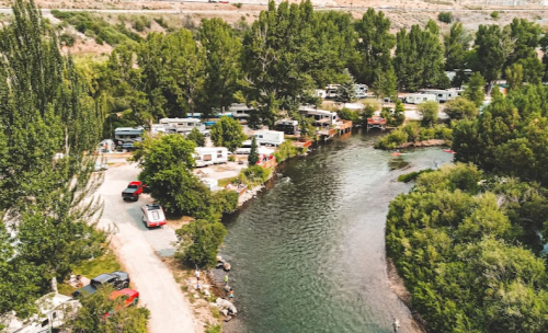 Aerial view of a campground by a river, featuring RVs, trees, and a winding waterway.