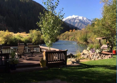 Scenic riverside view with a deck, chairs, and mountains in the background under a clear blue sky.