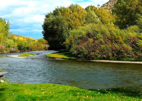 A serene river winding through lush greenery and trees under a partly cloudy sky.