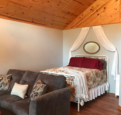 Cozy bedroom with a bed draped in white fabric, a gray sofa, and wooden ceiling accents.