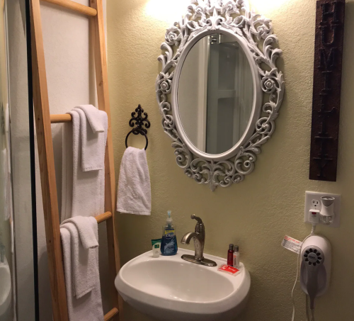 A small bathroom featuring a decorative mirror, sink, towels, and a wooden ladder for storage.