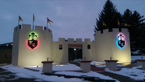 A snow-covered castle entrance with colorful illuminated shields and flags, set against a twilight sky.