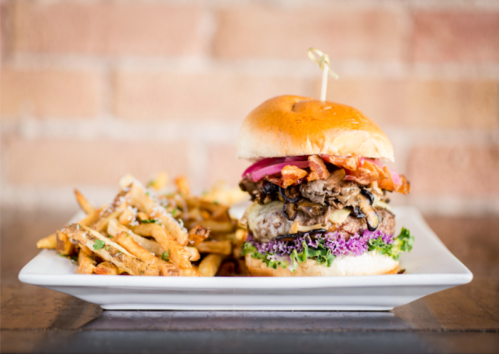 A gourmet burger stacked with toppings, served with a side of crispy fries on a white plate.