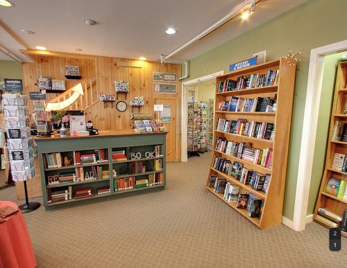 Cozy bookstore interior with wooden shelves, a checkout counter, and a variety of books displayed.