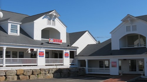 Two white buildings with gray roofs, featuring porches and signs, set against a clear blue sky.