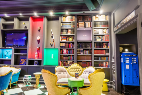 A stylish lounge with colorful seating, a bookshelf, and a blue police box in the corner.