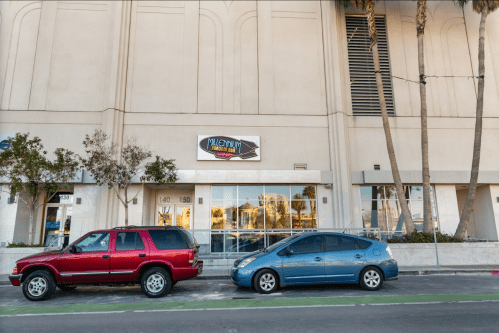 Two parked cars, a red SUV and a blue hatchback, in front of a building with a sign for "Kelsey’s." Palm trees nearby.