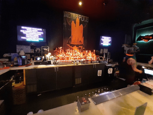 A dimly lit bar with a vibrant display of bottles and a Metropolis-themed poster on the wall.