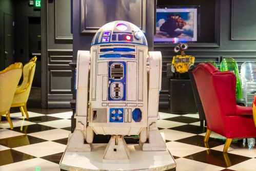 A vintage R2-D2 droid stands in a stylish room with black and white checkered flooring and colorful furniture.