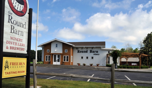 Exterior view of the Round Barn Winery, Distillery, and Brewery with a sign and tasting room in a rural setting.