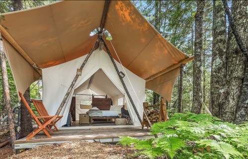 A cozy glamping tent nestled in a forest, featuring a wooden deck and rustic furnishings.