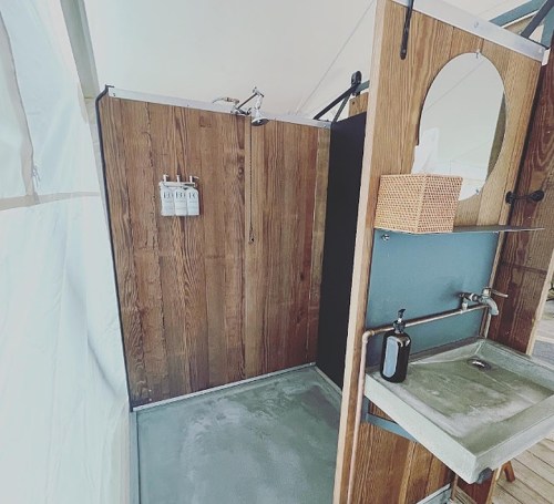A modern shower area with wooden walls, a concrete floor, and a stylish sink with a mirror and storage basket.