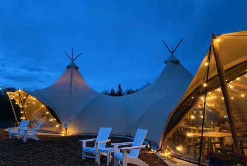 A cozy outdoor space with illuminated tents and white chairs, set against a twilight sky.