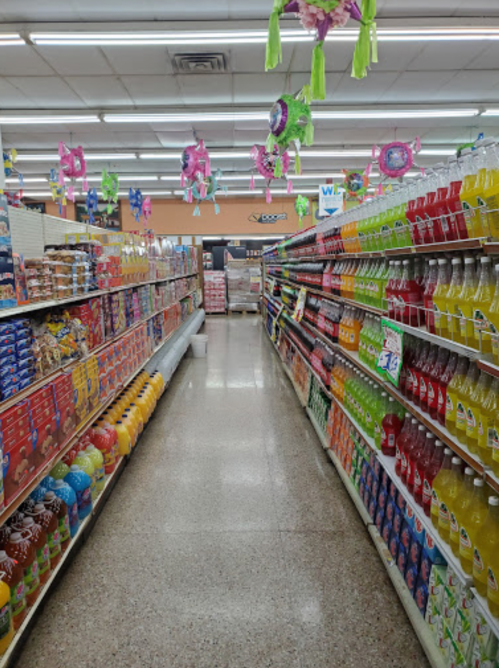 A grocery store aisle lined with colorful snacks and beverages, decorated with festive piñatas overhead.
