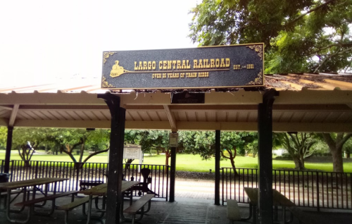 Sign for Largo Central Railroad, established in 1911, displayed at a picnic area with trees in the background.