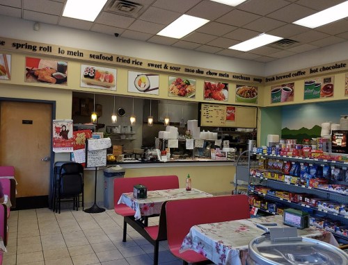 Interior of a casual restaurant with tables, a menu on the wall, and a counter displaying food items.