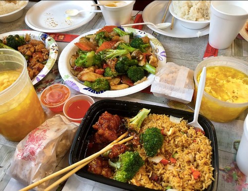 A table filled with various Chinese dishes, including fried rice, chicken, vegetables, and sauces in takeout containers.