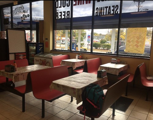 Interior of a casual diner with empty red booths and tables, large windows showing a street view outside.