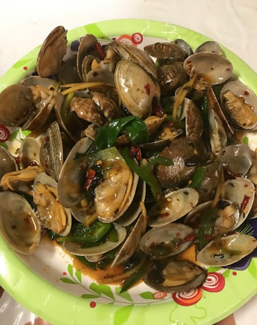 A plate of cooked clams with green onions and spices, garnished with red chili flakes.