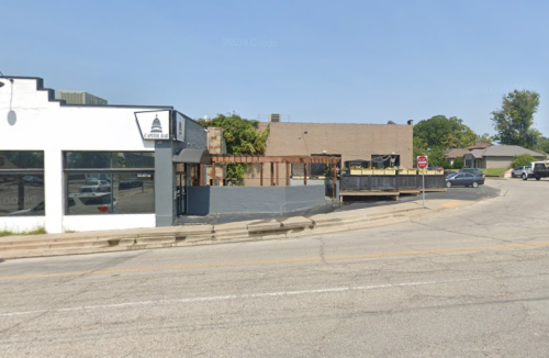 A street view of a corner with a white building and a vacant lot, under clear blue skies.