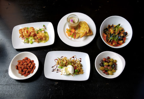 A variety of dishes on white plates, including seafood, pasta, dessert, and mixed nuts, arranged on a dark table.