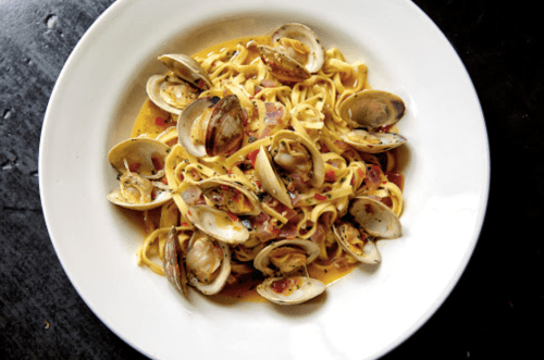 A bowl of pasta with clams in a creamy sauce, garnished with herbs and spices.