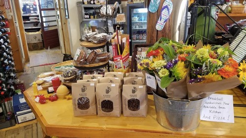 A cozy shop display featuring coffee bags, baked goods, and a bouquet of flowers on a wooden counter.