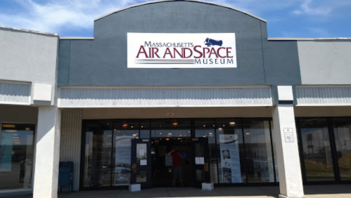 Exterior of the Massachusetts Air and Space Museum, featuring a large sign and glass entrance. Clear blue sky above.