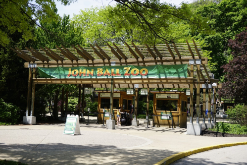 Entrance to John Ball Zoo, featuring a wooden archway and ticket booths surrounded by lush greenery.