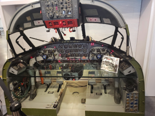Cockpit of a vintage aircraft, featuring numerous controls, gauges, and a flight manual on the dashboard.