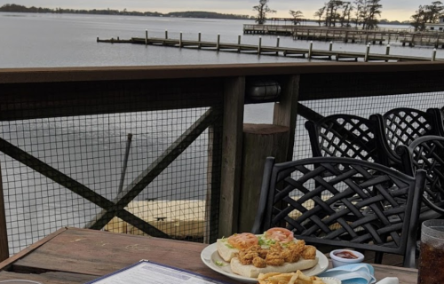 A scenic view of a lake with a plate of fried shrimp, fries, and a menu on a wooden table.