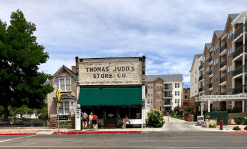 Historic store front with "Thomas Judd's Store Co." sign, surrounded by modern buildings and trees.