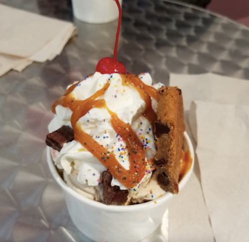 A delicious ice cream sundae topped with whipped cream, a cherry, caramel drizzle, sprinkles, and cookie pieces.